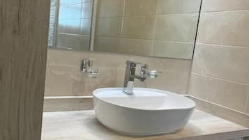 A modern bathroom with a round white sink, a mirror above it, and light-colored wooden cabinetry.