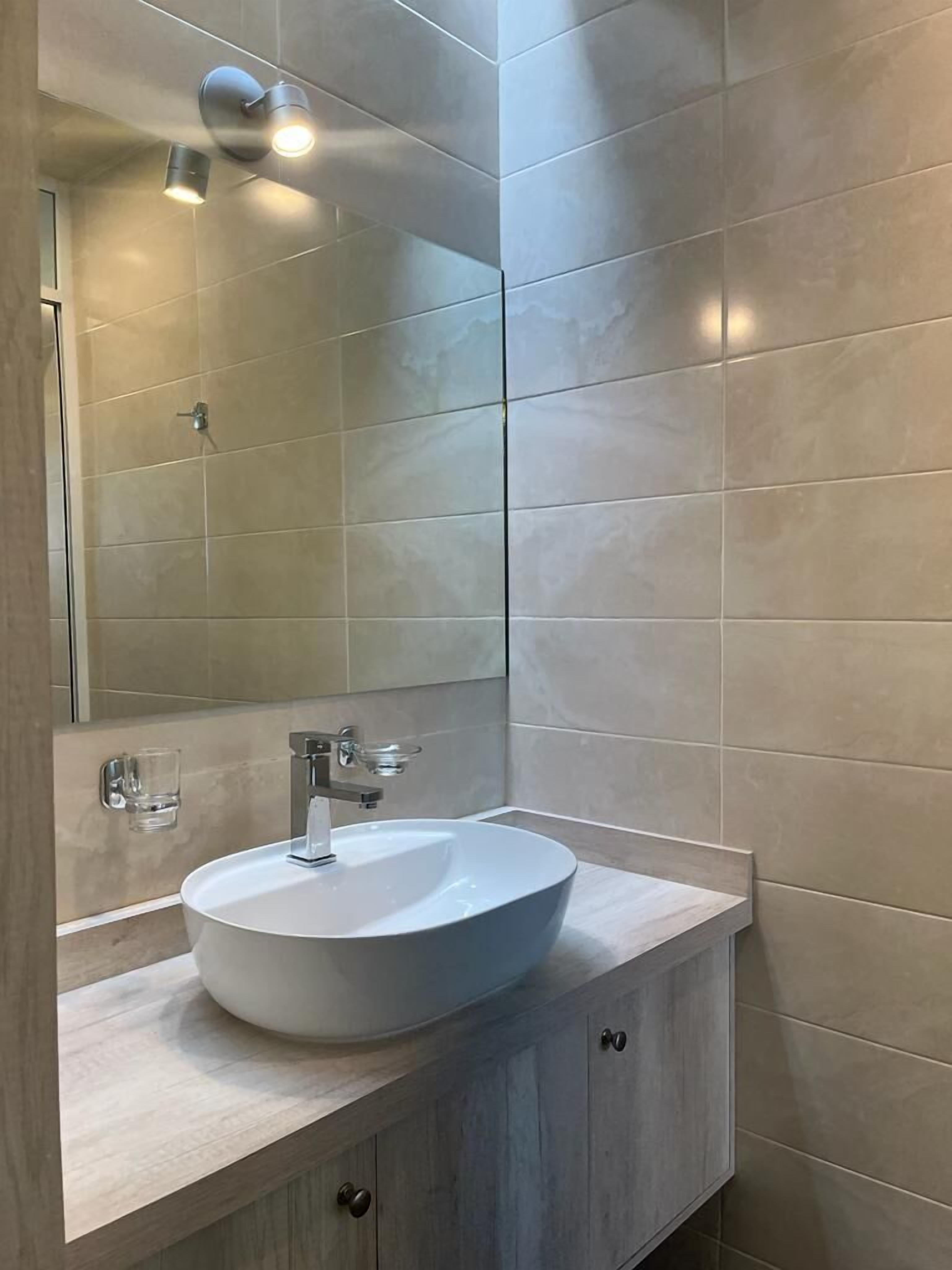 A bathroom with a white sink, a mirror, and a light fixture above the mirror.