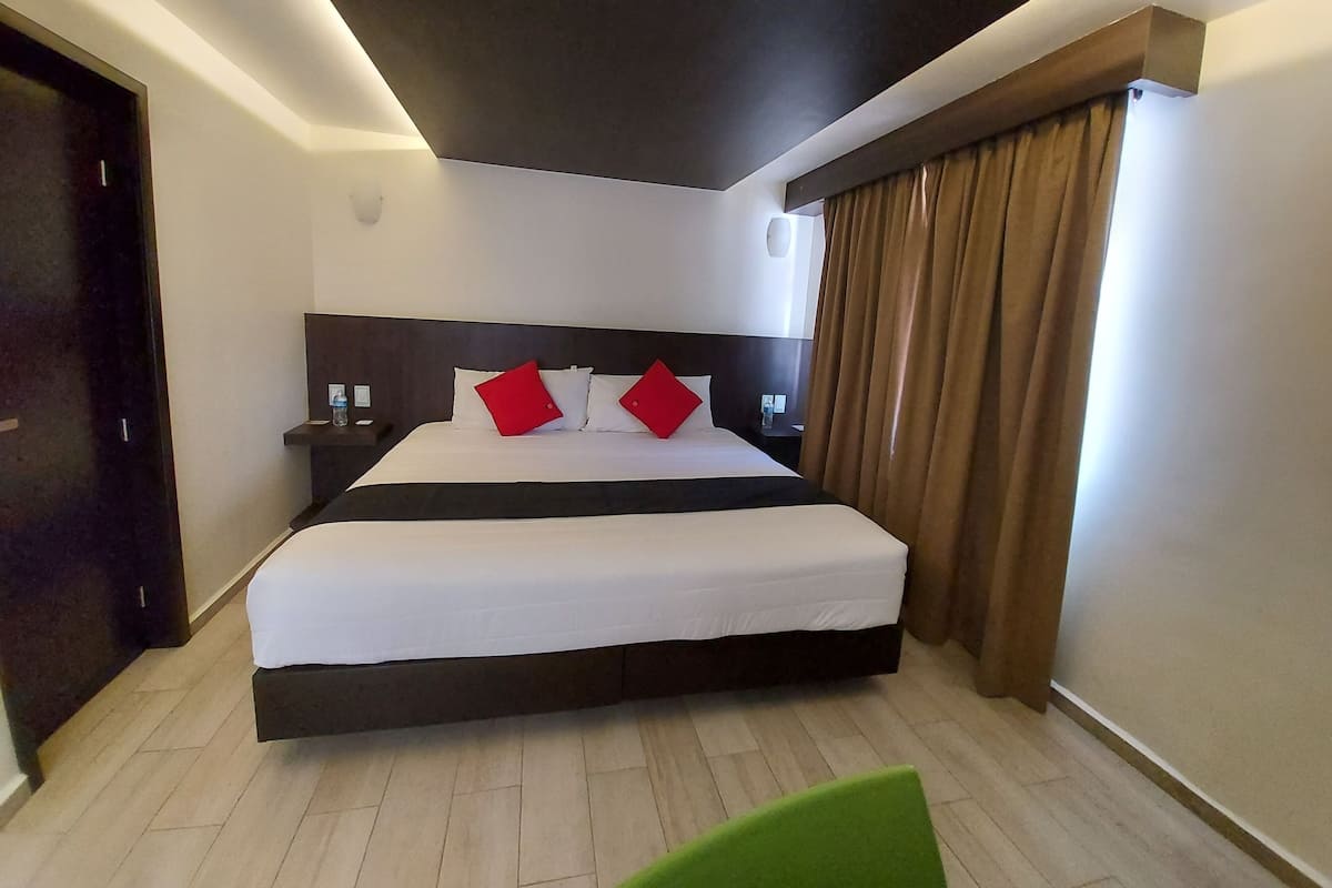 Een moderne hotelkamer met een groot bed, een donker hoofdeinde en een groene stoel.