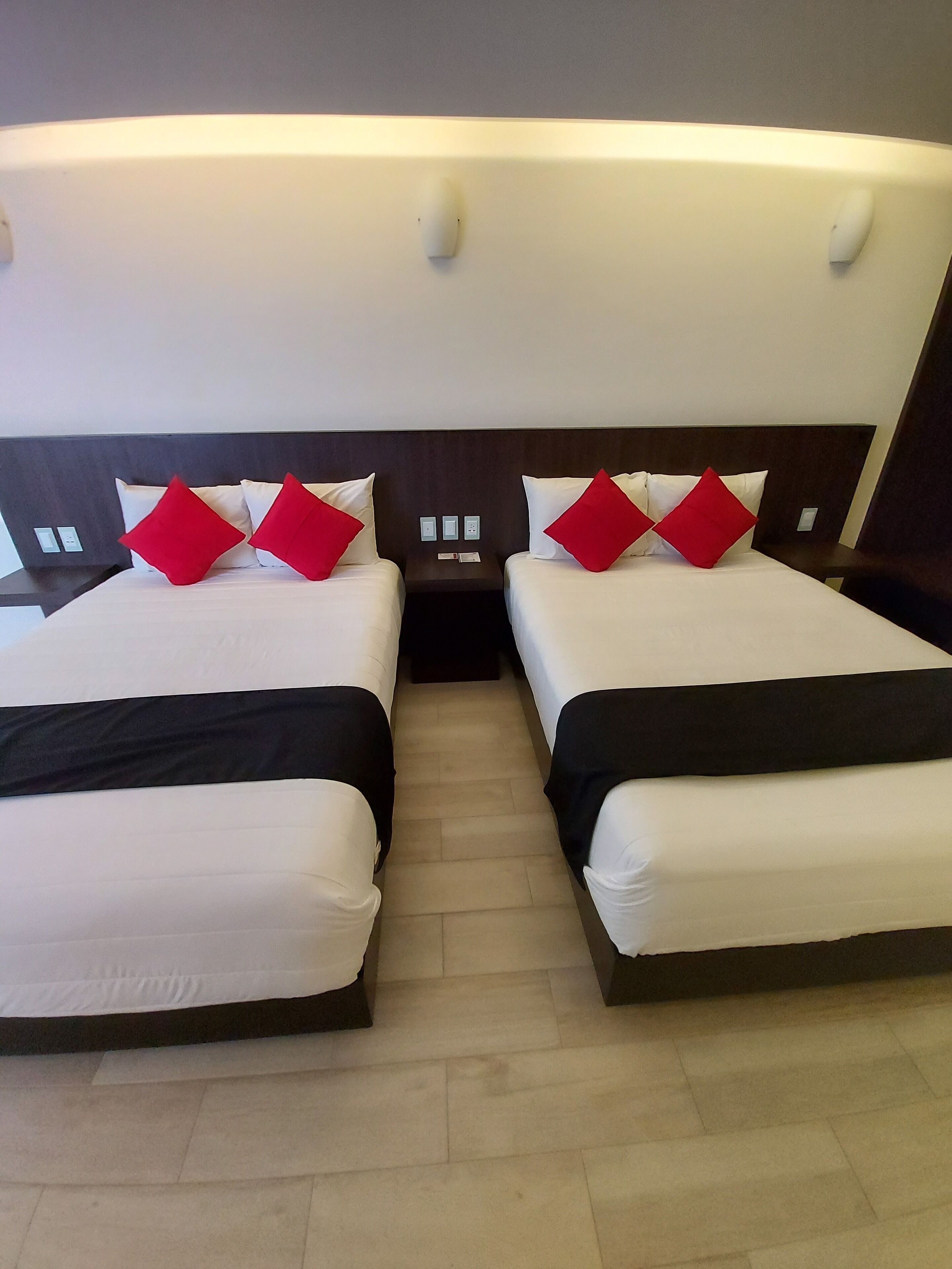 Een hotelkamer met twee bedden, elk voorzien van witte lakens en rode kussens.
