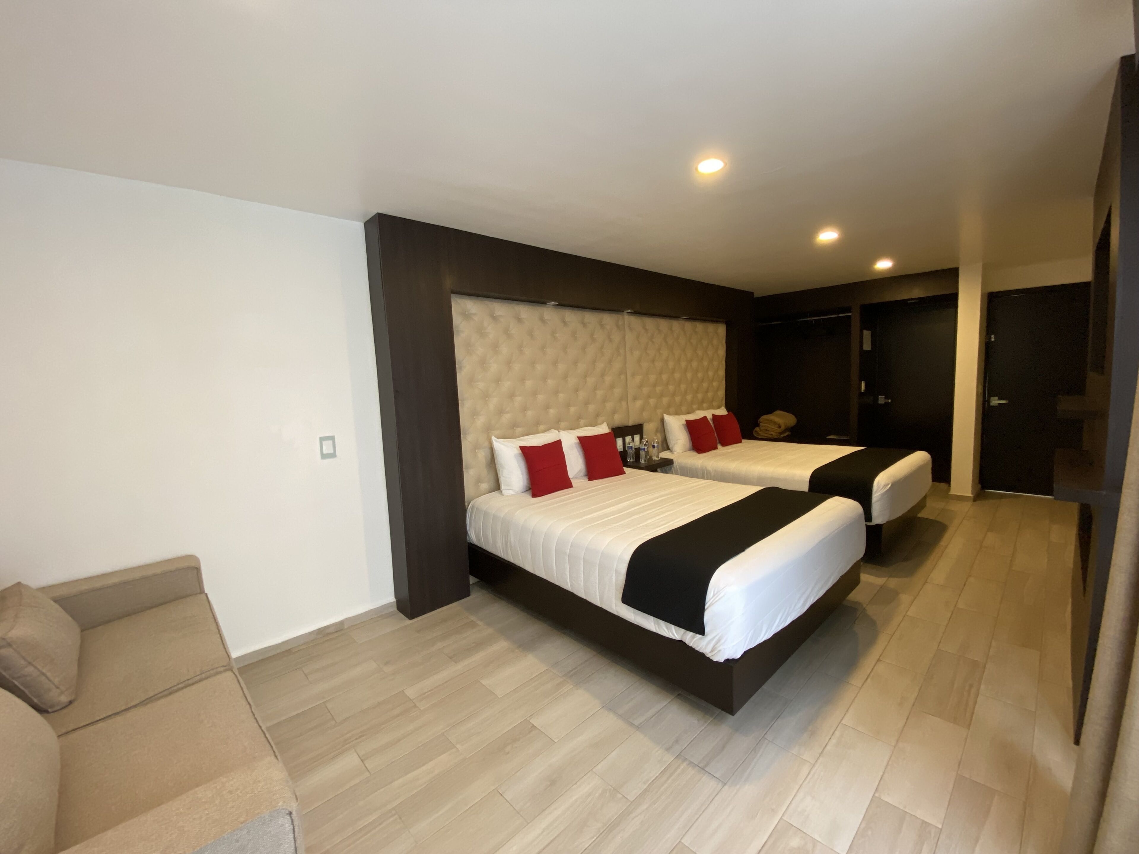 A modern hotel room with two beds, a sofa, and a wardrobe.