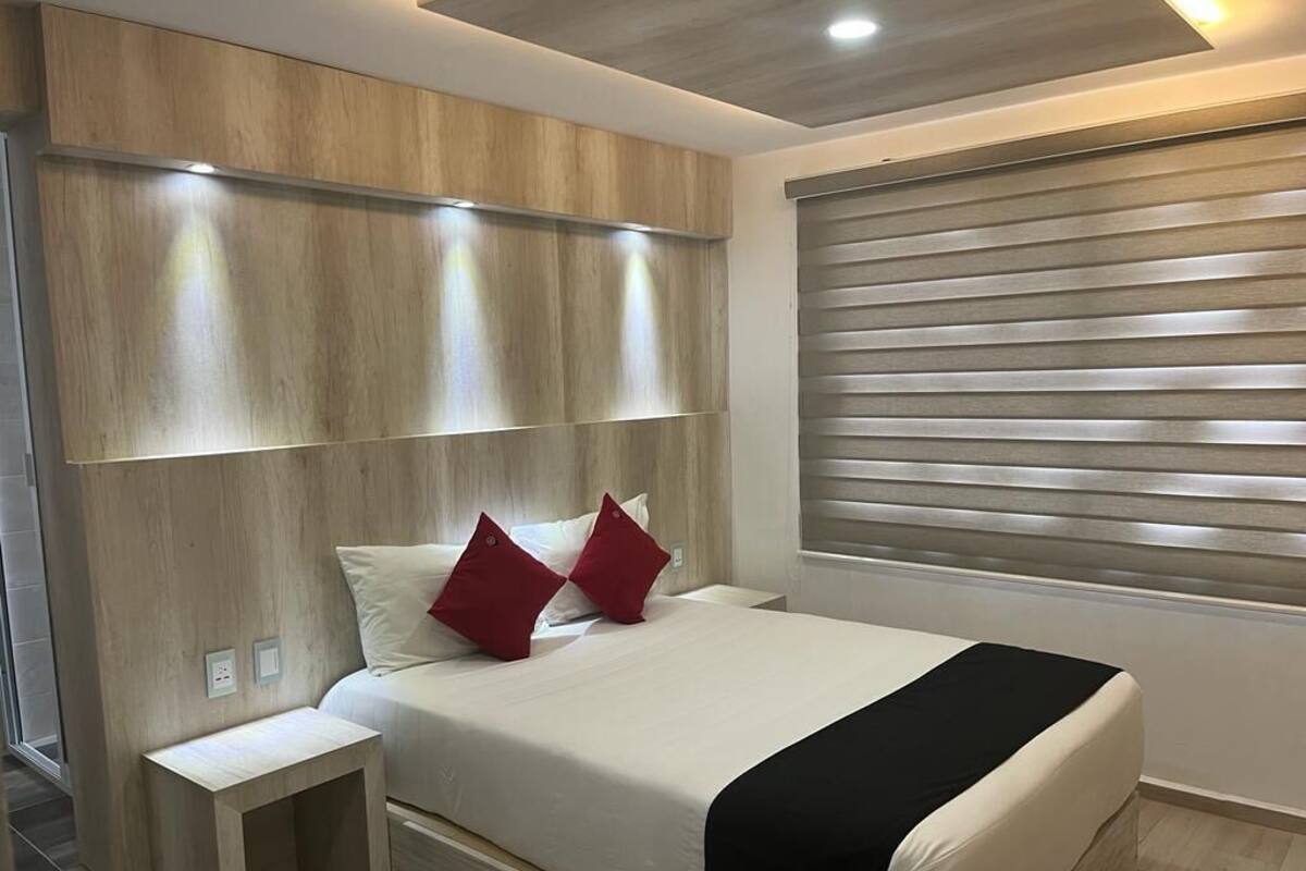 Een moderne slaapkamer met een houten hoofdbord, een nachtkastje en een raam met zonwering.