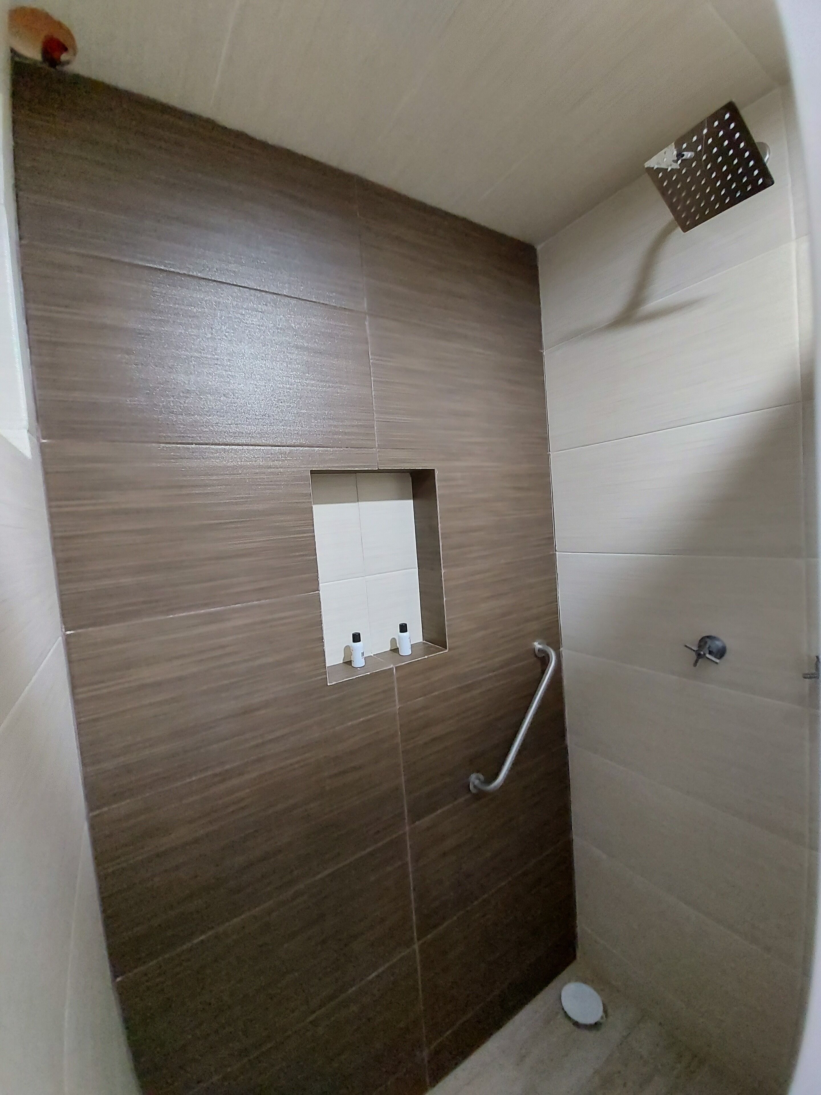 A small, enclosed shower area with a wooden panel wall, a white tiled section, and a metal grab bar.