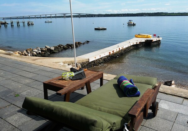 Un salón junto al agua con una mesa de madera, un sillón verde y un kayak amarillo.