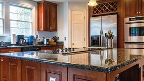 Una cocina moderna con encimeras de granito, armarios de madera y electrodomésticos de acero inoxidable, con iluminación colgante.