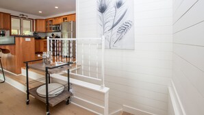 A kitchen with wooden cabinets, a stainless steel refrigerator, and a dining area with a white railing.