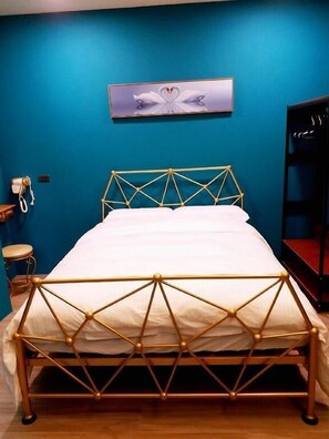 A bed with a geometric metal frame, a white mattress, and a blue wall with a heart-shaped artwork above it.