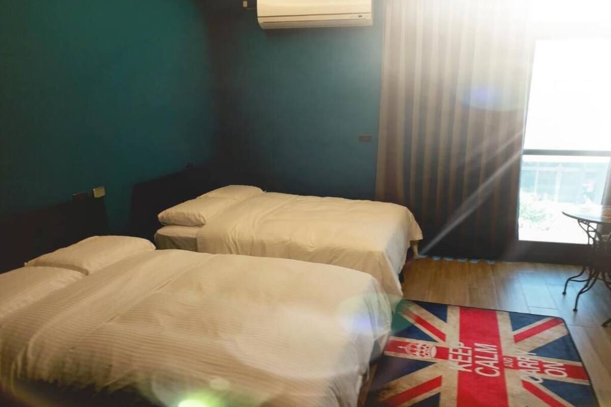 A hotel room with two beds, a view of the outdoors, and a Union Jack-themed rug.