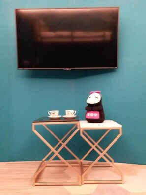 A room with a large flat-screen TV mounted on the wall, a small wooden table with two cups, and a panda-shaped object on the table.