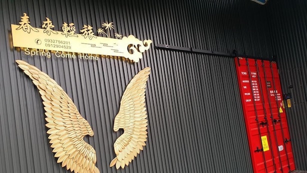 Una pared con una escultura de una ala dorada y un letrero con caracteres chinos y texto en inglés.