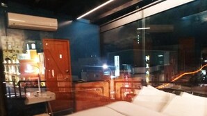 Una habitación de hotel con cama, una mesita y una silla. Se ve una ventana con vistas a la ciudad de noche.
