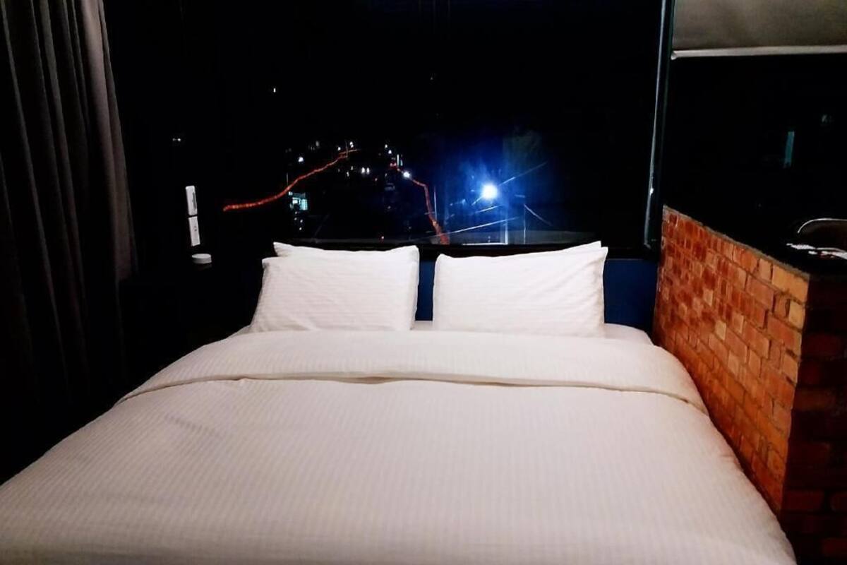 A hotel room with a bed, a brick accent wall, and a view of city lights at night.