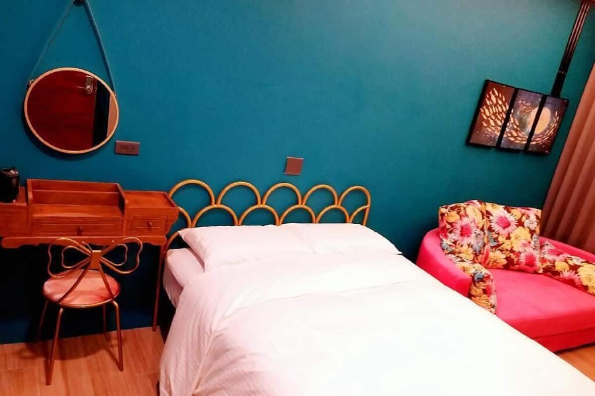 A bedroom with a bed, a desk, a chair, a mirror, and a sofa.