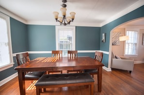 A dining room with a wooden table and chairs, a bench, a chandelier, and a window with blinds. - 2 Bedroom-Sleeps 5-Only 5 Blocks to the Square and MTSU! (Murfreesboro)