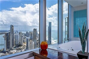 A modern hotel room with a large window offering a cityscape view, a bathtub, and a decorative vase on the windowsill.
