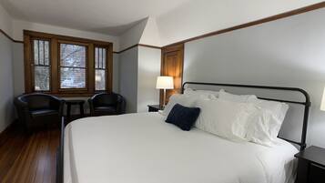 A hotel room with a large bed, two chairs, a desk, and a window with blinds.