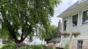 A residential garden with a stone retaining wall, various plants, and hanging flower baskets. - Exceptional new listing Decorah Craftsman Bungalow (Decorah)
