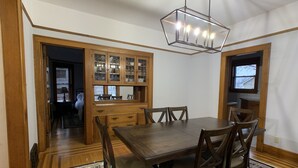 A dining area with a wooden table and chairs, a chandelier, and a kitchen with wooden cabinets and a window. - Exceptional new listing Decorah Craftsman Bungalow (Decorah)