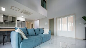 Una sala moderna con un sofá seccional azul, una zona de cocina y un amplio ventanal corredizo que da a un balcón.