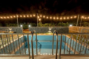 Ein Schwimmbad mit Steinmauer und Metallgeländern, umgeben von Grünpflanzen und Lichterketten.