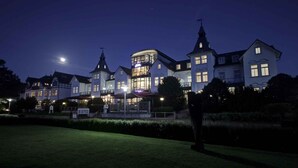 A large, historic building with multiple wings and a prominent tower, featuring a well-lit entrance and a landscaped garden area. - Holiday home with WIFI and terrace (Damp)