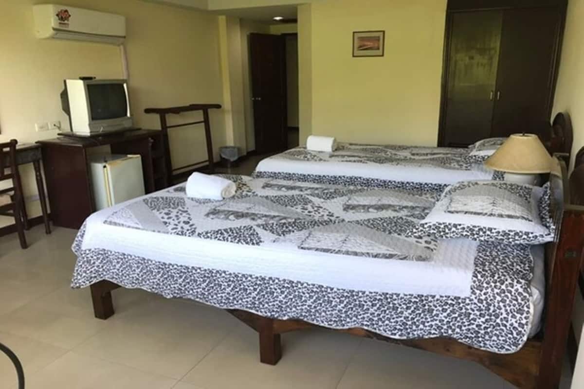 A hotel room with two beds, a television, a desk, and a refrigerator.