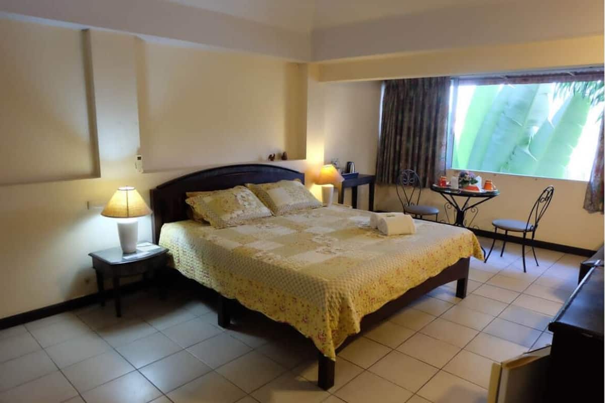 A hotel room with a large bed, two bedside lamps, a small table with a chair, and a window with curtains.