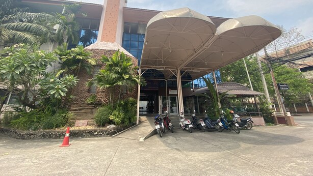 A building with a large covered entrance, a tall chimney, and several parked motorcycles. - OYO 903 Madame Kim Hostel (Lampang)