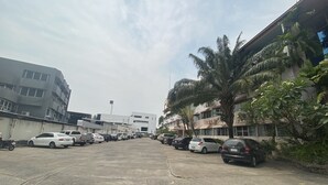 A parking lot with various cars and a building with balconies and palm trees. - OYO 903 Madame Kim Hostel (Lampang)
