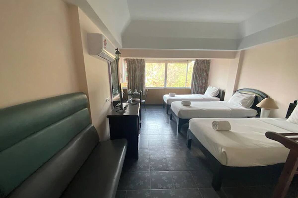 A hotel room with a green sofa, two single beds, a desk with a computer, and a window with curtains.