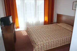 Ein Hotelzimmer mit einem Bett, einem Fernseher auf einer Holzkommode und einem Fenster mit Vorhängen.