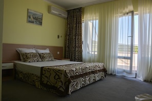 Ein Hotelzimmer mit einem großen Bett, einem Fenster mit Vorhängen, einem Gemälde an der Wand und einer Klimaanlage.