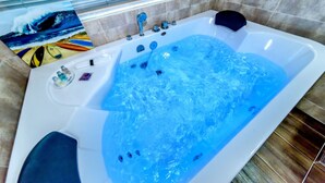 A large, rectangular hot tub with multiple jets, a small sink, and a window with blinds. - Swimeong Spa Pension (Seogwipo)