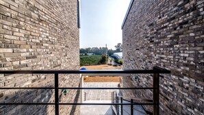 A narrow corridor with brick walls and a metal railing, leading to an outdoor area with a pathway and greenery. - Swimeong Spa Pension (Seogwipo)