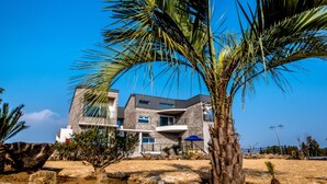 A modern two-story building with a stone facade, large windows, and a balcony. - Swimeong Spa Pension (Seogwipo)