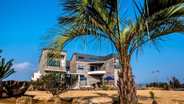 A modern two-story building with a stone facade, large windows, and a balcony. - Swimeong Spa Pension (Seogwipo)