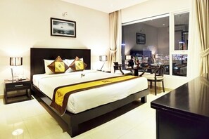 Une chambre d’hôtel avec un grand lit, un bureau et une vue sur la ville la nuit.