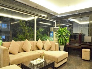 A modern living room with a beige sectional sofa, a coffee table with a tray, and a large potted plant.