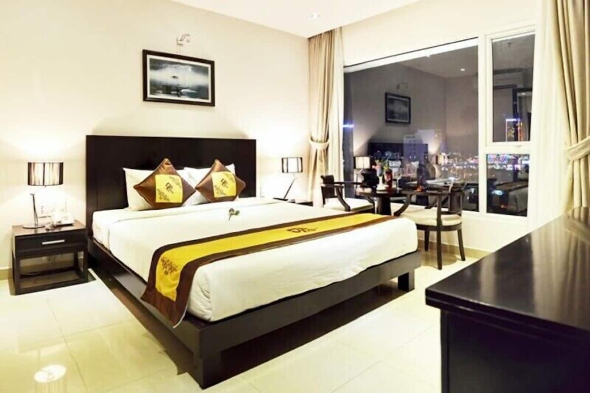 Une chambre d’hôtel avec un grand lit, un bureau et une vue sur la ville la nuit.