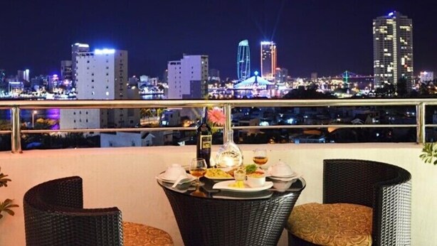 A balcony with a table set for dining, overlooking a city skyline at night. - D&C Hotel Danang (Da Nang Municipality)