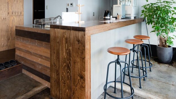 Una cocina moderna con una isla de madera, taburetes de bar, iluminación colgante y una planta en maceta.