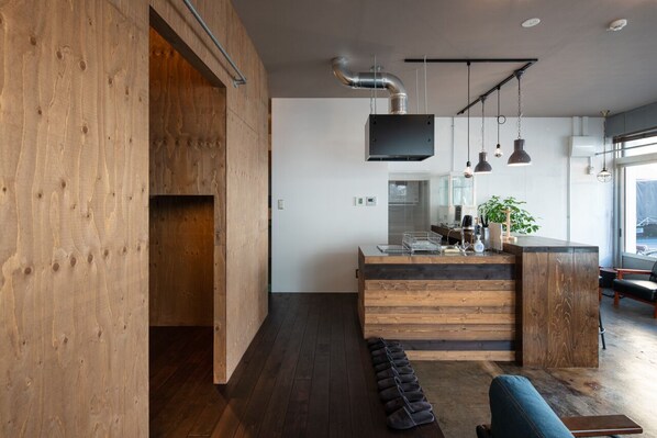 A modern kitchen with wooden cabinetry, a central island, pendant lighting, and a large window providing natural light.