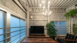 A modern living room with a large flat-screen TV, wooden furniture, and a chandelier. - Rakuna Inn Yu Kinshicho (Tokyo)