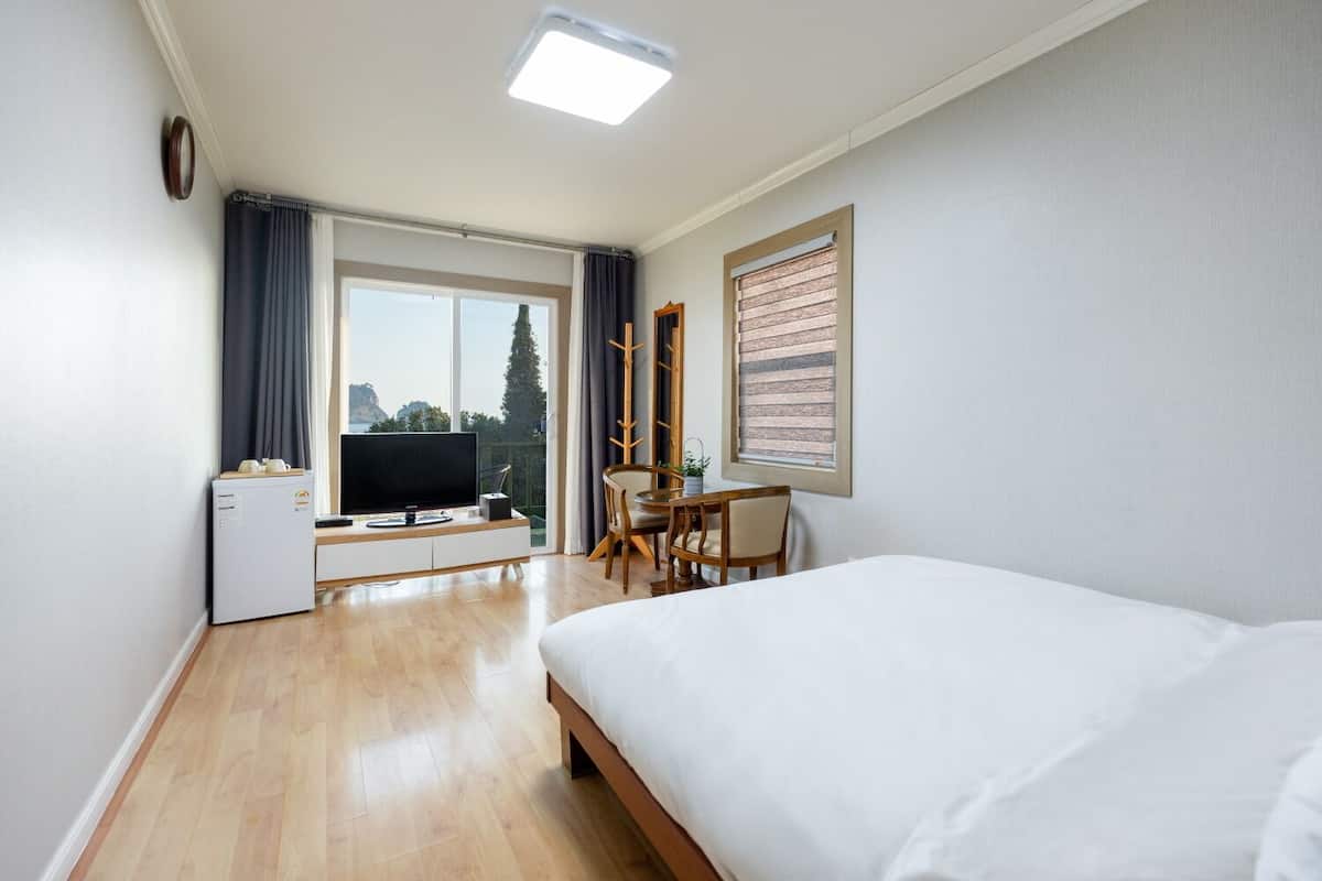 A hotel room with a bed, a desk with a chair, a television, and a small refrigerator.