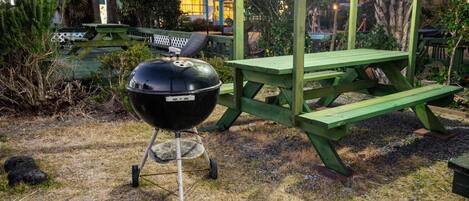 A barbecue grill with a wooden table and benches in a garden setting.