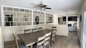 A dining area with a wooden table and chairs, a ceiling fan, and a view into the kitchen.