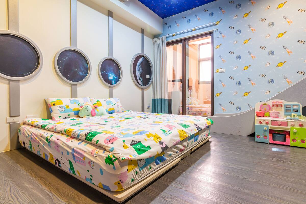 Un dormitorio con cama, ventana, un reloj de pared y un juego de cocina para niños.