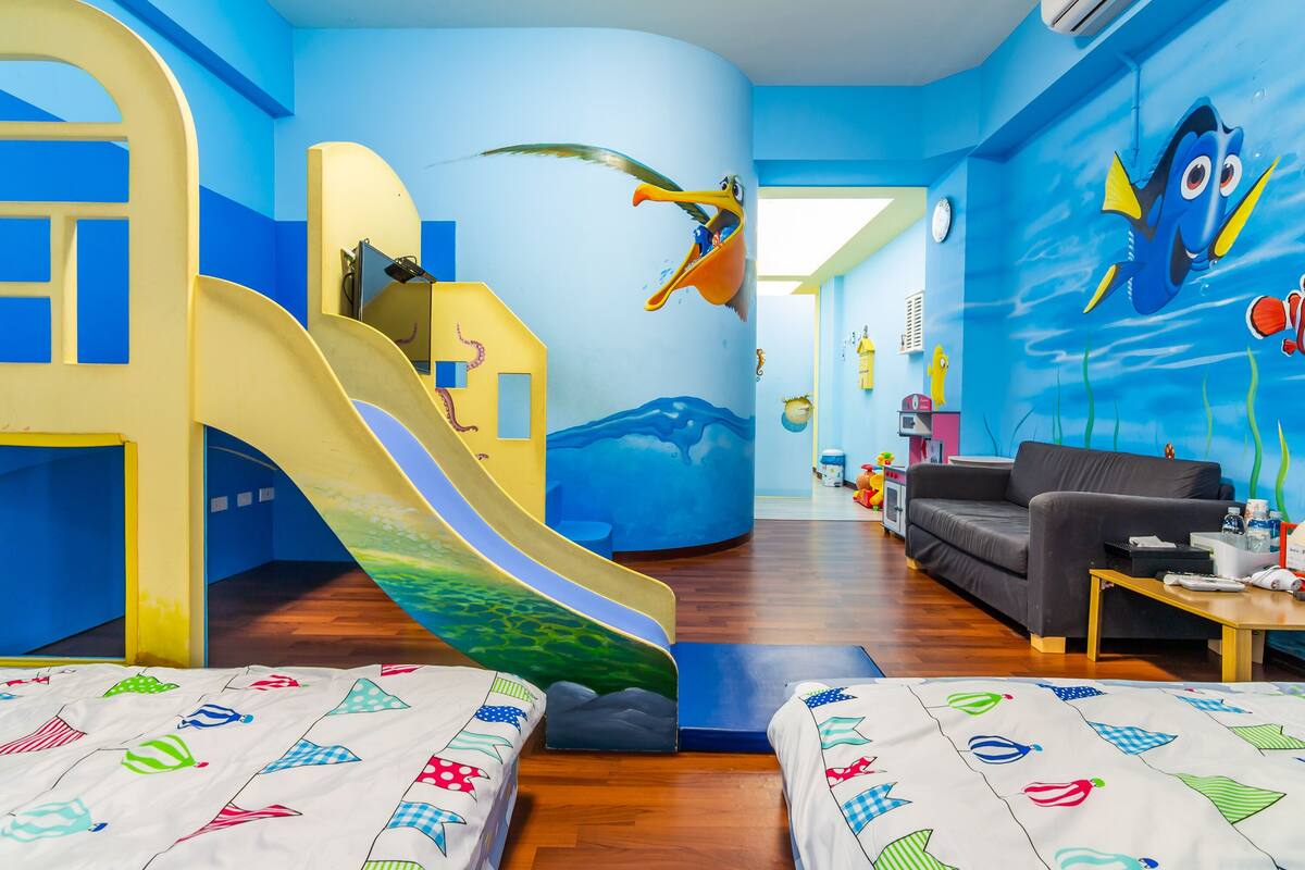 Una sala de juegos para niños, con un tobogán, un sofá y un mural en la pared.