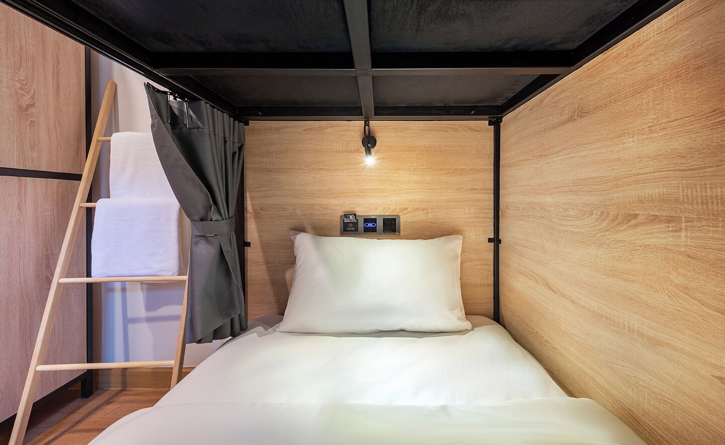 Een kleine kamer met een bed, een houten garderobe, een trapje en een klein plankje met een lamp.