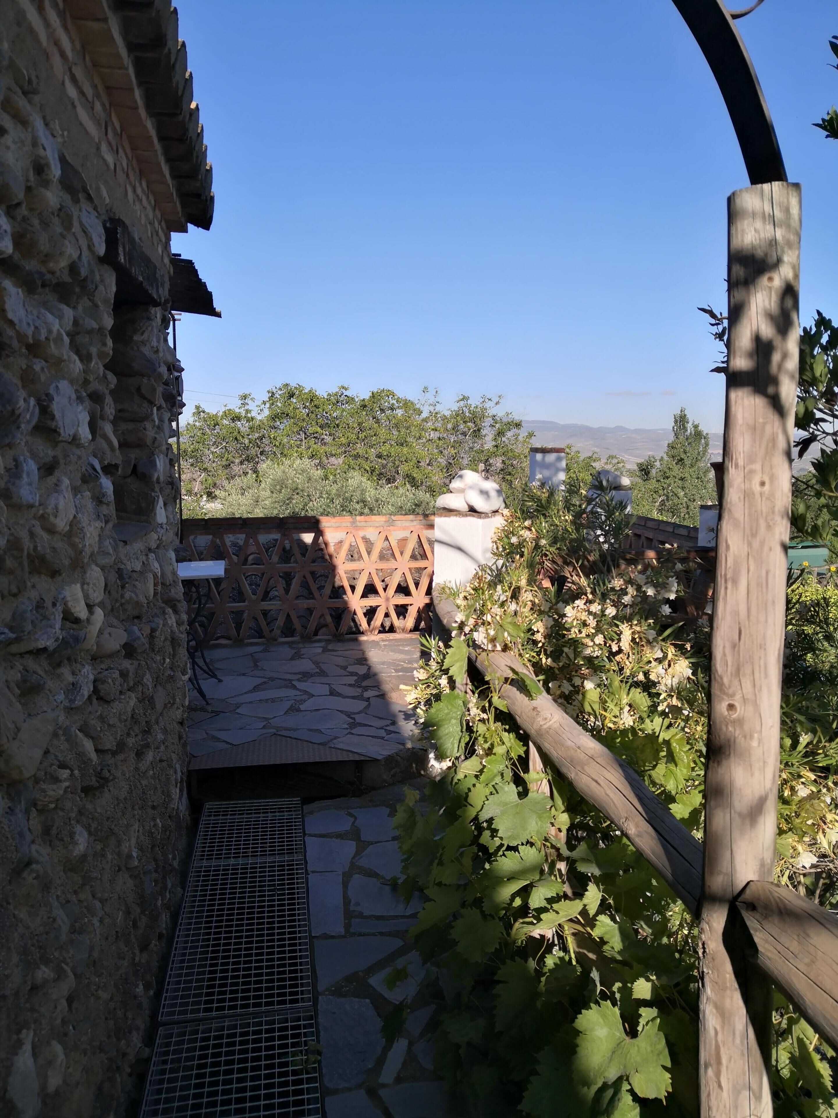 Edificio de piedra con entrada de reja metálica, cerca de madera y vistas a colinas distantes.